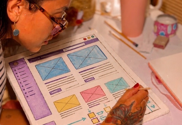 Nathalia pintando um wireframe de interface em canvas, no ateliê